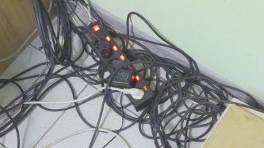 Aktif göstergeleri olan bir güç şeridine bağlı elektrik kabloları bir duvarın yakınındaki düzensizliğe dağılmış..