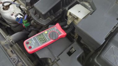 Motor bölmesindeki klemp metre kullanarak, dijital ekranda değerleri gösteren bir araçtaki mevcut ölçüm.