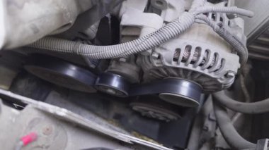 Motor bölmesinde görünür sürücü kemeri ve makaraları olan bir araba alternatörünün çalışması, mekanik bir sistem gösteriyor.