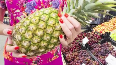 A pineapple in a womans hands against a fruit display window.
