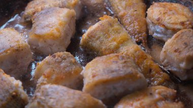 Bir tavada kızaran balık parçalarının yakın çekimi altın kahverengiye kadar, görünür yağ ile.