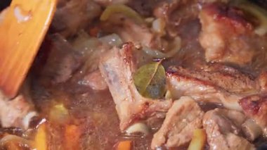 Yakın plan soğan ve baharatla kızartılmış et pirzolası, ahşap bir spatulayla karıştırılıyor.