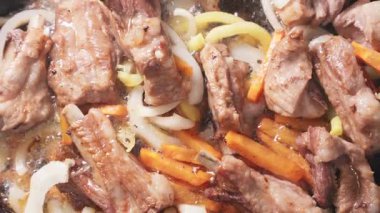 Kızartma tavasında soğan ve havuçla cızırdayan et yakın plan.