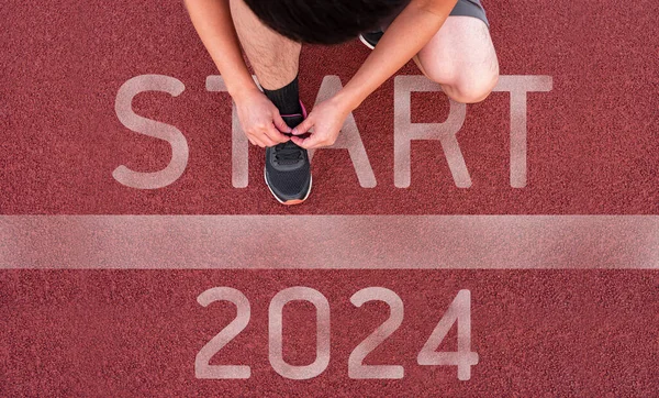 Close up of man shoe on an athletics track engraved with the year 2024 and START. Beginning and start of the new year 2024, goals and plans for the next year concept.