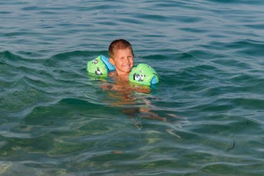 Mutlu çocuk denizde kol bandıyla yüzerken eğleniyor..