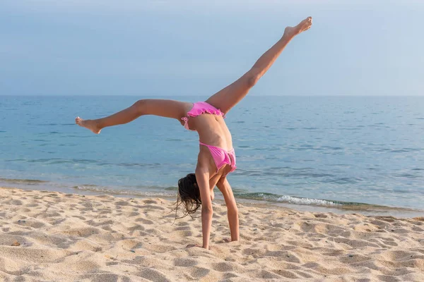 Sahilde bir çocuk spor yapıyor ve denizin arka planında jimnastik yapıyor. Bir çocuk sahilde amuda kalkar.