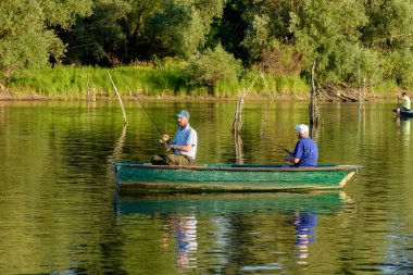 Novi Sad, Sırbistan - 06 Temmuz 2022: Sırbistan 'ın Novi Sad kenti yakınlarındaki Tuna Adası (Sodros). Balıkçılar kayıkta oturup olta tutuyorlar..