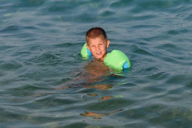 Mutlu çocuk denizde kol bandıyla yüzerken eğleniyor..