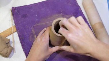 Sanatçı kadın kilden bir ürün yapıyor, elleri yakın, kille çalışıyor.