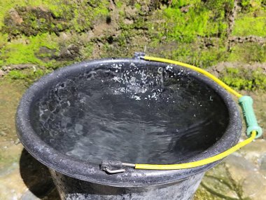 Eski siyah kova temiz suyla dolu.