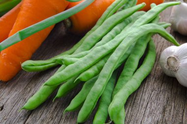 Ahşap masa üstünde havuçlu taze yeşil sebzeler.