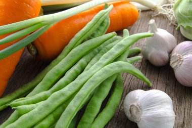 Ahşap masa üstünde havuçlu taze yeşil sebzeler.