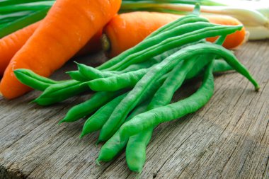 Ahşap masa üstünde havuçlu taze yeşil sebzeler.