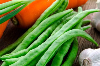 Ahşap masa üstünde havuçlu taze yeşil sebzeler.