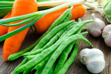 Ahşap masa üstünde havuçlu taze yeşil sebzeler.