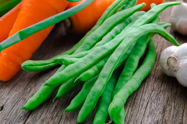 Ahşap masa üstünde havuçlu taze yeşil sebzeler.