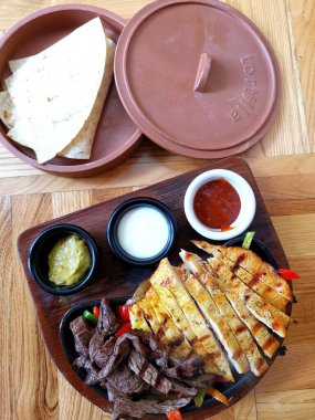 grilled beef and chicken with sauce and vegetables on wooden table