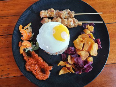 Fried Rice with chicken satay, egg and Vegetables Nasi Goreng on a black plate