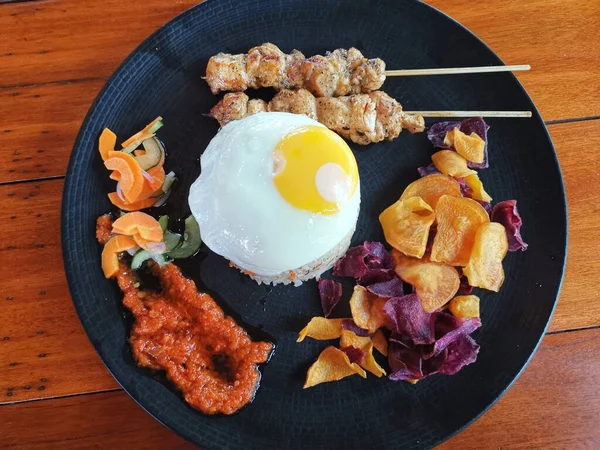 Fried Rice with chicken satay, egg and Vegetables Nasi Goreng on a black plate