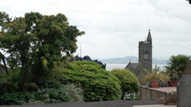 BURNTISLAND, FIFE, İngiltere - 13 Haziran 2024: Burntisland, Fife 'da yeşil ağaçlı bir bahçeden bir kilisenin ve Forth' un manzarası.