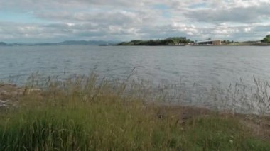 BURNTISLAND, FIFE, SCOTLAND, UK - 11 Haziran 2024: Burntisland, Fife, sahilden manzaralı bir manzara. Sakin su bulutlu gökyüzünü yansıtır ve kıyı yeşil uzun otlarla kaplıdır..