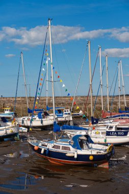 EDINBURGH - JULY 28, 2024: Several sailboats decorated with flags rest in a calm Fisherrow Harbour, surrounded by pink clouds and gentle water ripples, creating a serene seaside atmosphere. clipart