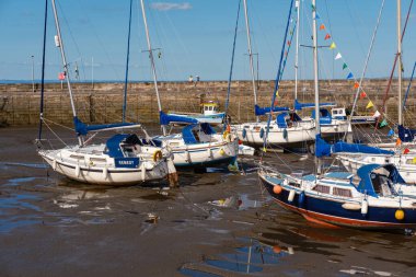 EDINBURGH - 28 Temmuz 2024: Balıkçı Limanı 'nda birkaç tekne demirlemiş, gelgit çekildikçe çamurda dinlenirken, birkaç kişi yakındaki iskelede güneşli havanın tadını çıkarırken.