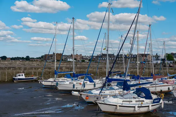 stock image EDINBURGH - JULY 28, 2024: Sailboats are moored peacefully in Fisherrow Harbour, surrounded by a tranquil waterway and a bright blue sky dotted with fluffy white clouds.