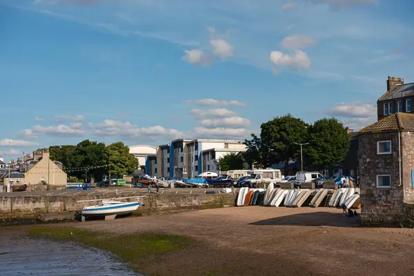 stock image EDINBURGH - JULY 28, 2024: A series of boats rest on the sand as the tide recedes, with modern buildings and trees visible in the background on a sunny day in Fisherrow.