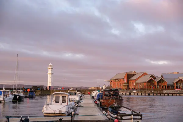 stock image The sunset casts a warm glow over Newhaven Harbour in Edinburgh, featuring a lighthouse and boats peacefully docked along the wooden pier as the day ends.