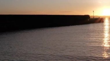 BURNTISLAND, FIFE, SCOTLAND, İngiltere - 4 HAZİRAN 2025: Sakin suların üzerine altın renkler dökerek Burntisland Batı İskelesi Deniz fenerinin geniş açılı, sakin bir atmosferini oluşturan nefes kesici günbatımı.