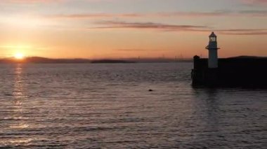 BURNTISLAND, FIFE, SCOTLAND, İngiltere - 4 HAZİRAN 2025: Gün batımında fok, tekne ve deniz feneri silueti, Dördüncü Su Firth ve Burntisland Batı İskelesi Feneri 'nin sakinleştirilmesi.