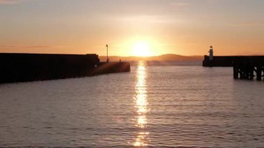 BURNTISLAND, FIFE, SCOTLAND, İngiltere - 4 HAZİRAN 2025: Gün batımının son ışınları Firth of Forth ve Burntisland Batı İskelesi Deniz fenerinin sakin sularında canlı renkler sergiliyor.