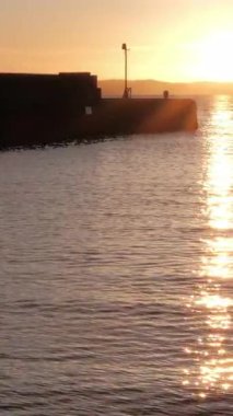 BURNTISLAND, FIFE, SCOTLAND, UK - 4 HAZİRAN 2025: Sakin sulara sıcak renkler dökme, Firth of Forth sahil şeridinin ve Burntisland Batı İskelesi Deniz fenerinin dingin güzelliğini vurguluyor