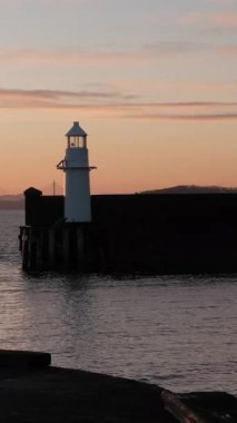 BURNTISLAND, FIFE, SCOTLAND, İngiltere - 4 HAZİRAN 2025: Güneş Firth of Forth 'un üzerinde batarken, deniz kenarında yürümek, sahil manzarasını ve Burntisland Batı İskelesi Deniz fenerini, dikey.