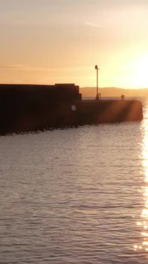 BURNTISLAND, FIFE, SCOTLAND, UK - 4 HAZİRAN 2025: Güneş batarken Burntisland limanının huzurlu güzelliği, su ve gökyüzü boyunca ılık altın renkler sergiliyor,.