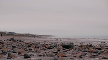 EDINBURGH, SCOTLAND, İngiltere - 5 HAZİRAN 2024: Sakin, bulutlu bir gün doğumu Portobello Sahili 'nde, kayalık kıyıların nazik dalgalarla buluştuğu, sahilde yürüyen insanlar.