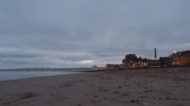 Portobello Sahili 'nde sakin bir sabah, bulutlu bir gün doğumu yansıması, şafak vakti kıyı şeridi ışıldarken, gece şehri.
