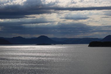 Kuzey Denizi 'nde gümüşi yansımalar, Bergen, Norveç yakınlarındaki dağ sıraları ve kasvetli gökyüzü.