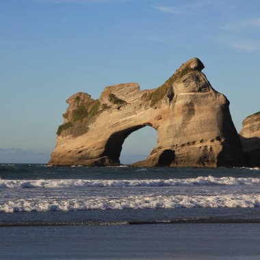 Wharariki Beach, Yeni Zelanda 'da büyük kaya kemeri ve dalgalar..