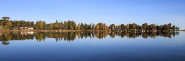 Colorful trees in autumn mirroring in Lake Vanern, Sweden. clipart