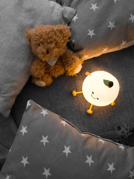 Kids\' night light among pillows and toys. Turned on the night light. Cozy shelter for a little toddler. A cute flashlight that illuminates the nursery room.