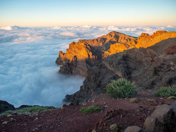 İspanya 'nın La Palma adasında sabah güneşinde bulutlardan süzülen kayalık dağlar. Caldera ters bulutların altında. Kayalık tepeli gün doğumu