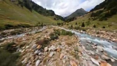 Taze dağ nehri deresi, bir FPV drone ile uçuyor. Macera yürüyüşü ormanı ve yeşil çayır vadisi.