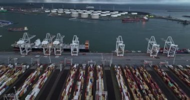 Aerial drone video of a bustling container terminal with large cargo ships and a cloudy sky in the background, showcasing the scale and activity of the modern shipping industry.