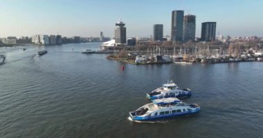 Amsterdam, 13th of February 2023, The Netherlands. See Amsterdams bustling Ij river and the essential role played by GVB ferries, all set against the stunning cityscape.