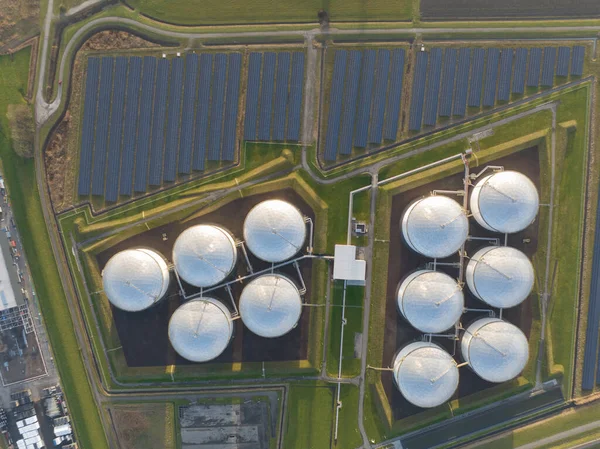 Witness the contrast between the old and new ways of energy production through a birds eye view of oil storage tanks and solar panels coexisting in a single location.