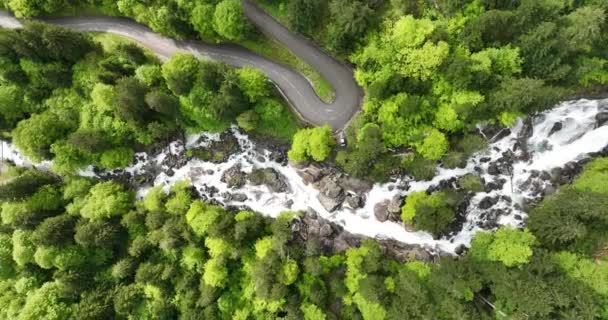 フランスの山々の滝の上から見下ろす空中ドローンのビデオとその隣にある曲がりくねったアスファルトの道路 — ストック動画