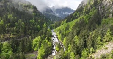Fransız Pireneleri 'nde bir şelalenin üzerinde uçmak, dağ manzarası, güneşli, sis ve yeşil ağaçlar. Fransız Pireneleri.
