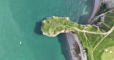 Tebeşirle kaplı tebeşirle kaplı ve deniz suyuna doğru çim akan tepeden aşağıya bakan bir drone videosu. Normandiya, Fransa